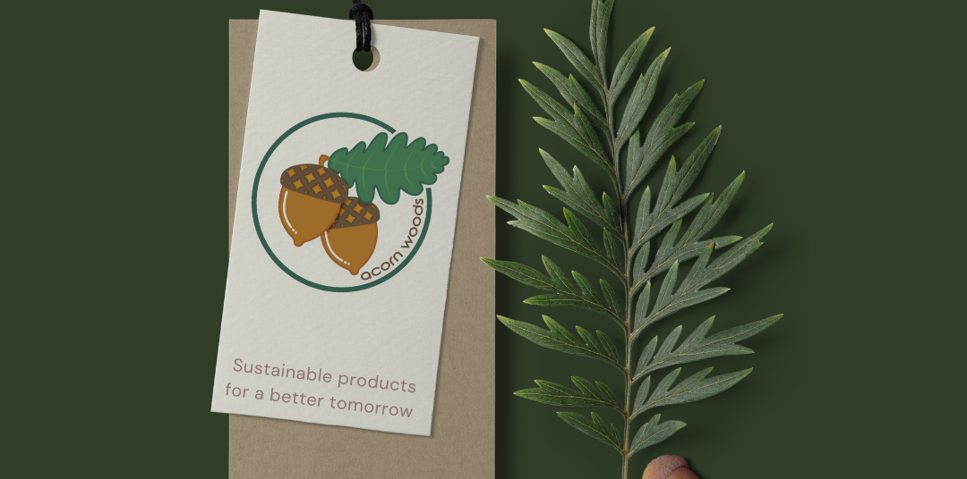 Acorn Woods logo on a recycled paper product tag layered on a brown paper tag on a background of green with a sprig of a fir tree and two acorns to the right.